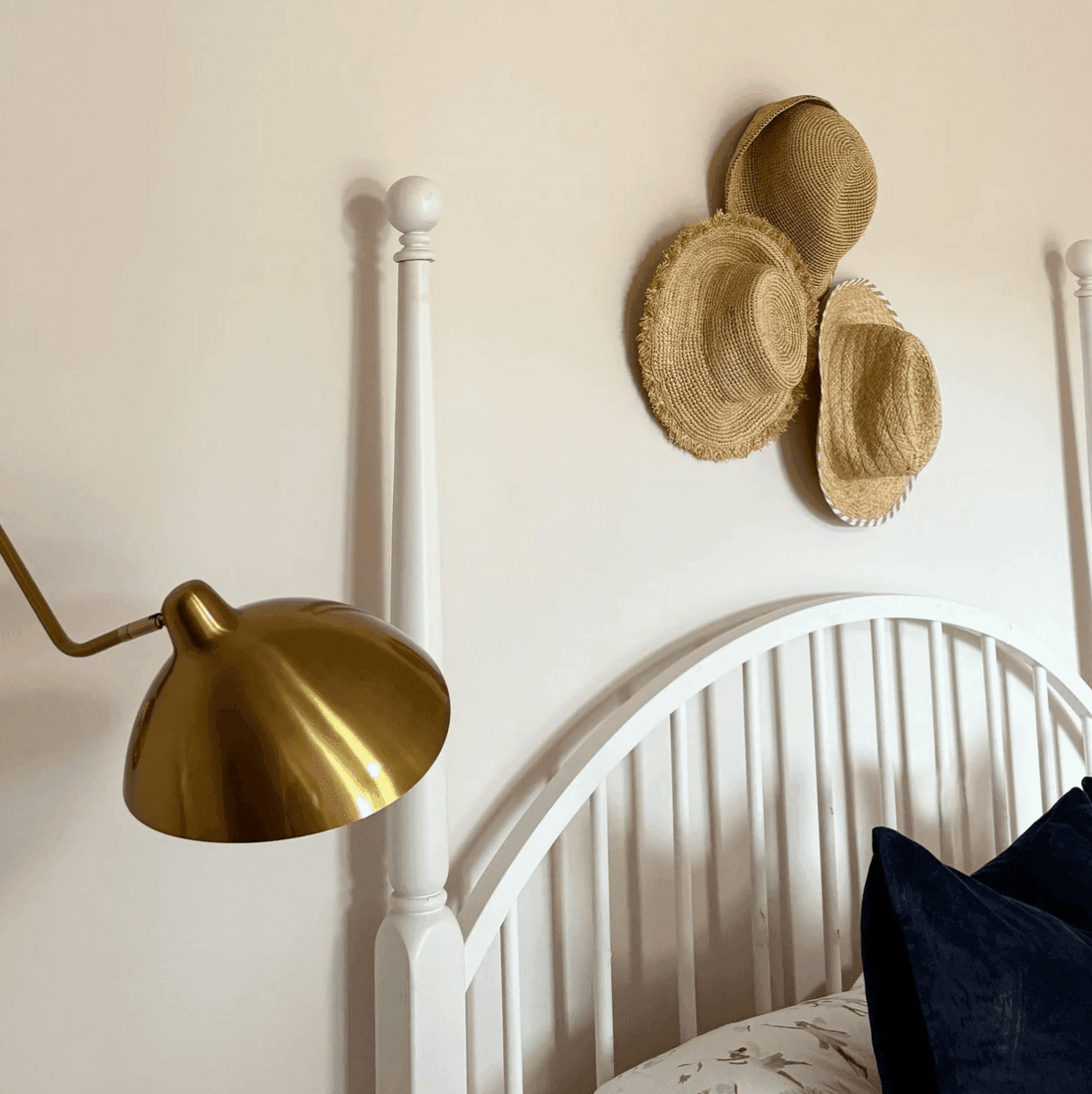 Bedroom designed with soft colors, brass sconce lights, bed, and hats hanging on the wall.